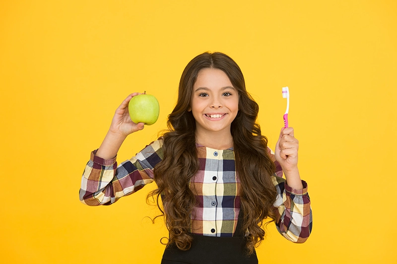 Smiling girl holding an apple and a toothbrush