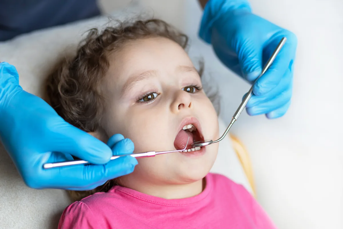 Pediatric dentist examining a young child's teeth and gums with a dental mirror and explorer