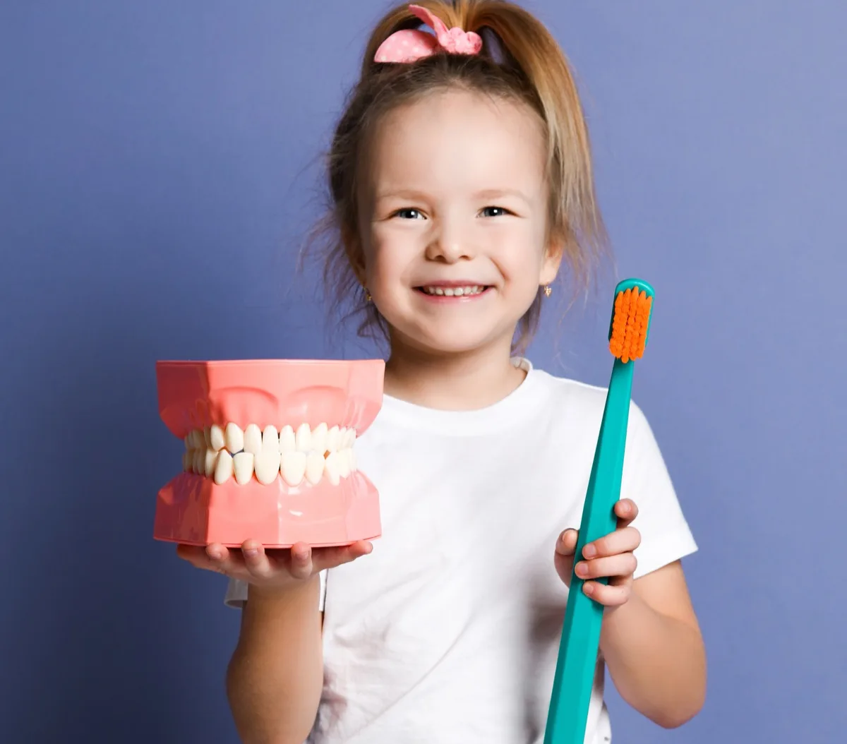 Smiling child holding a jaw model and toothbrush before a dental filling visit