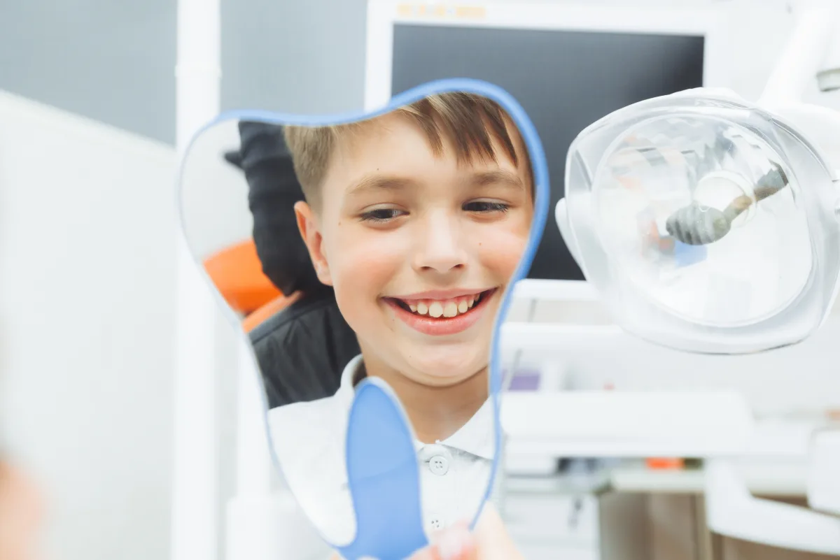 Smiling young patient holding a tooth-shaped mirror during a dental visit