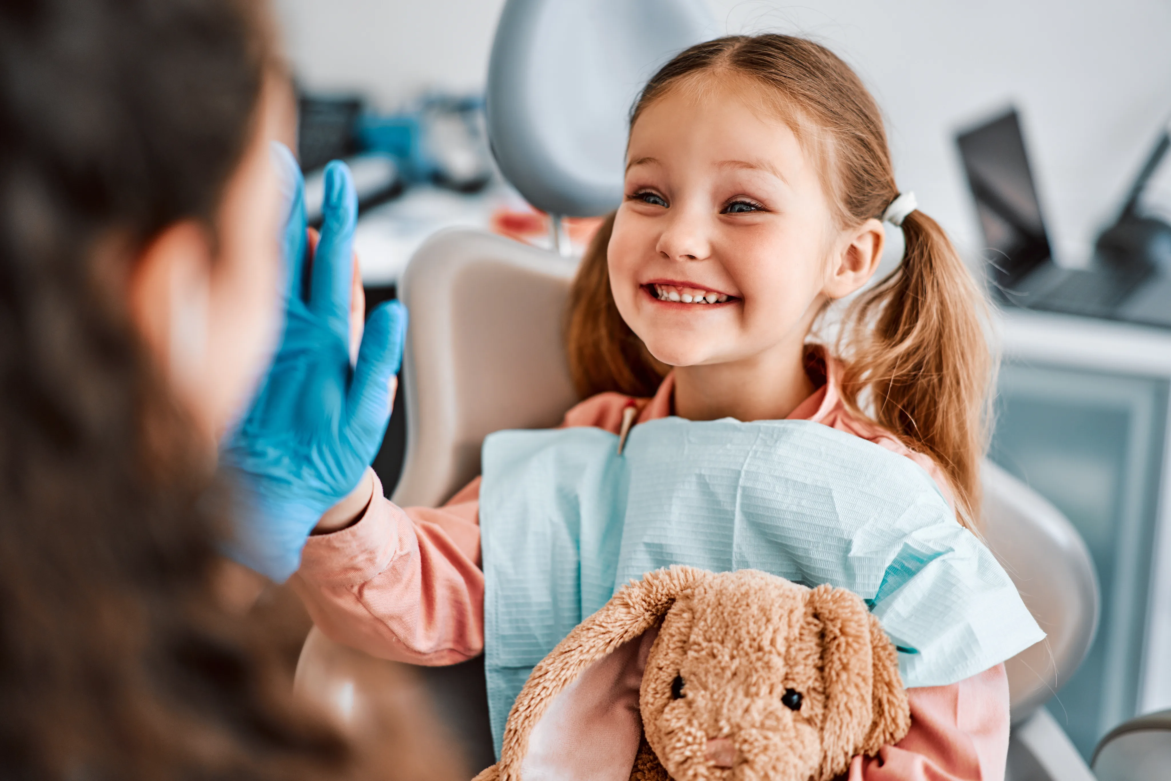 Smiling young patient high-fiving the dental team while holding a stuffed bunny