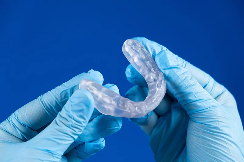 Gloved hands holding a clear oral appliance used to evaluate bite and jaw joint function