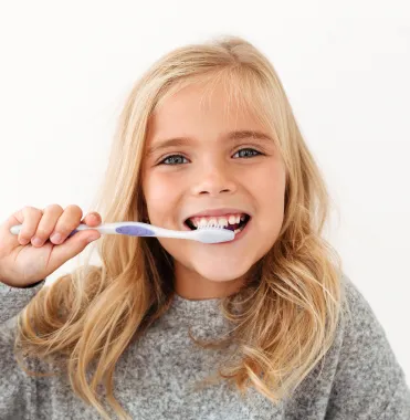 Smiling child brushing her teeth as part of fluoride-free, metal-free holistic care